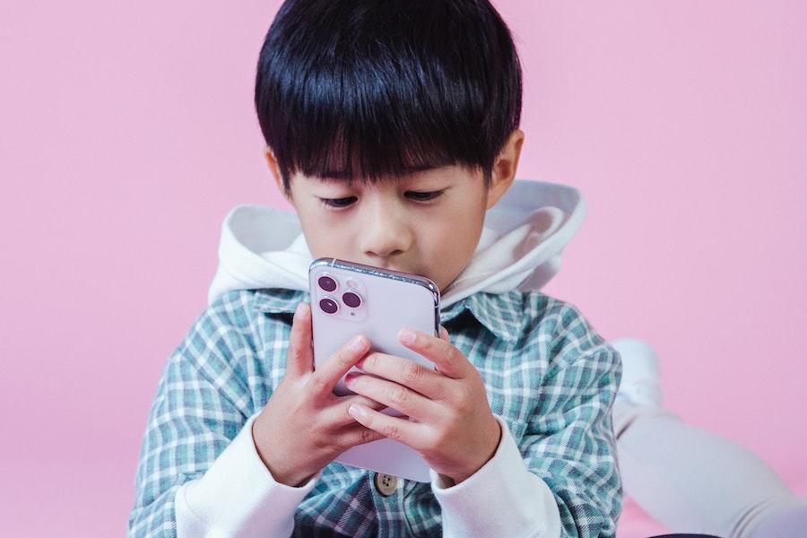 Een jongen die door een telefoon kijkt op een roze achtergrond